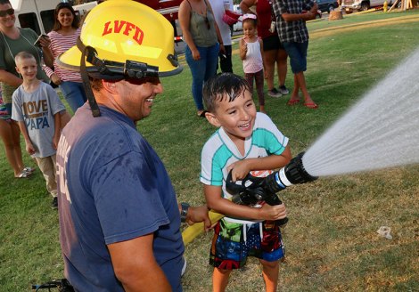 Lemoore Volunteer Fire Department firefighter Abi Shiyamura helps five-year-old Jesse Martinez cool down the crowd at the Neighborhood Watch event Tuesday.